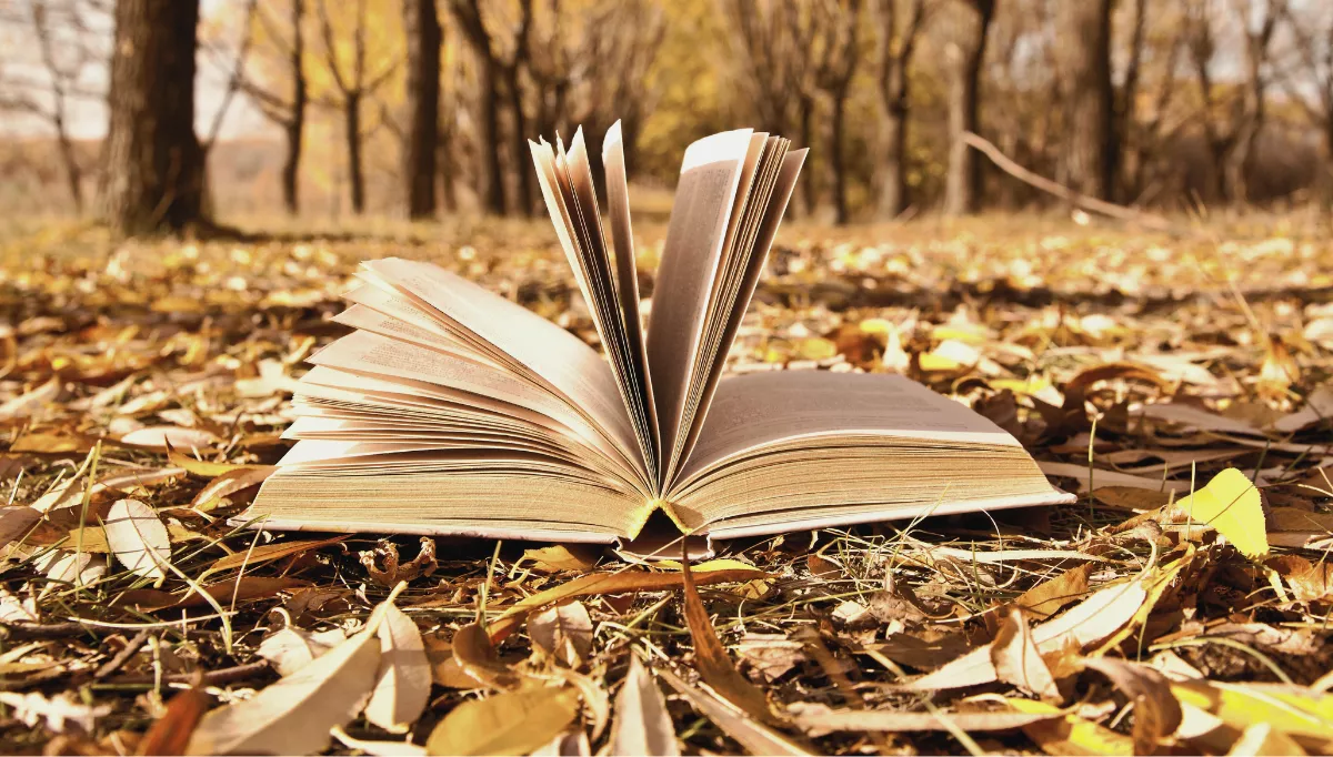 A book's pages flutter in the wind on an autumnal forest floor